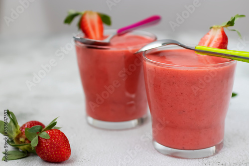 Organic strawberry smoothies in glass cups and ripe strawberries on a gray cement background.