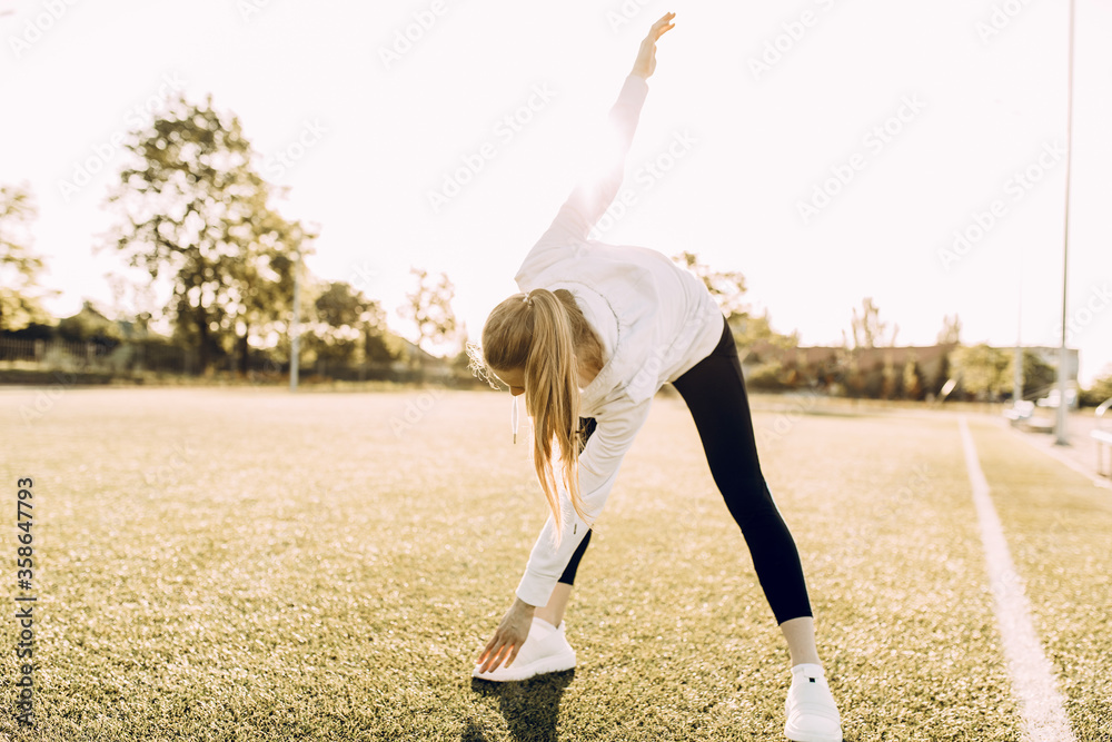 Young beautiful sports girl is engaged in sports at dawn in the stadium - obrazy, fototapety, plakaty 