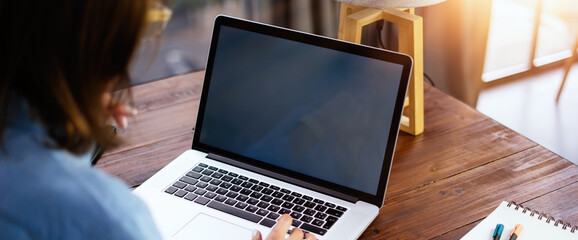 Mockup image of a woman using laptop with blank screen on wooden table