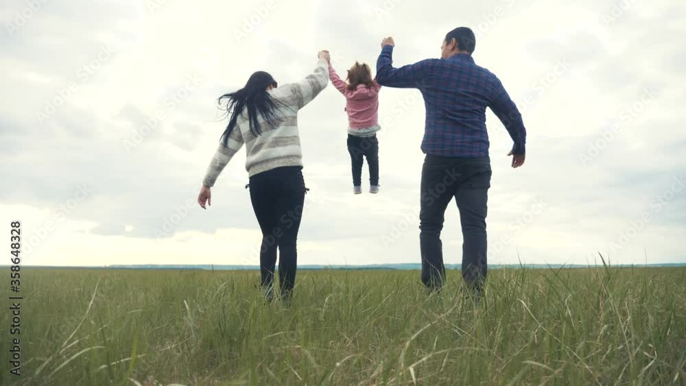happy family. mom dad and little child a are running in the park raise hands play teamwork outdoors holding hands. woman man and little girl raise up hands on green field at sunset lifestyle happy family. mom dad and little child a are running in the park raise hands play teamwork outdoors holding hands. woman man and little girl raise up hands on green field at sunset lifestyle