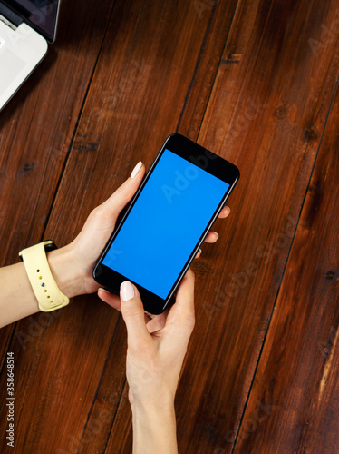 Mockup image of a woman using smartphone with blank screen on wooden table. Close up photo of female hands holding mobile phone vertically