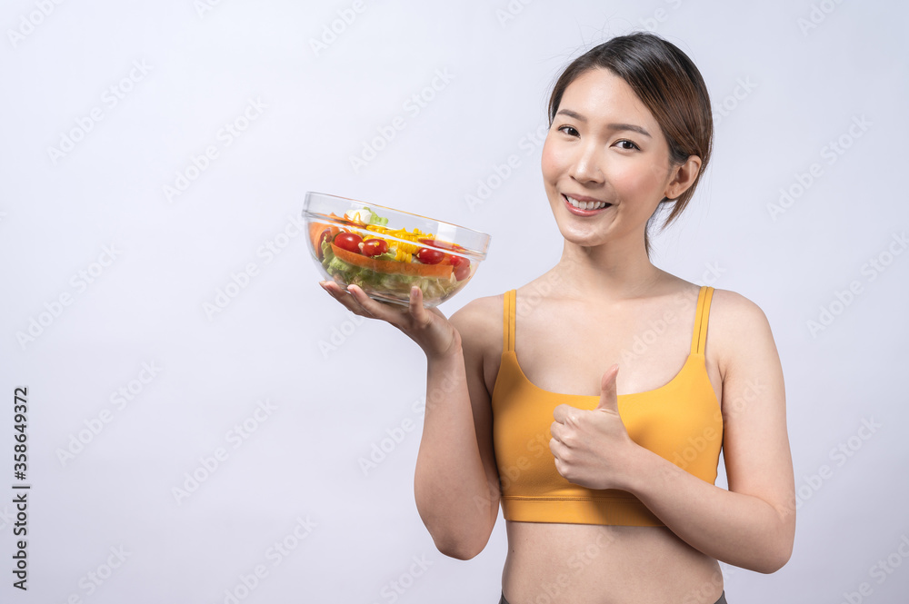 A sporty Asian woman in sportswear eating salad isolated on white background. concept of healthy lifestyle, vegetarian, wellbeing