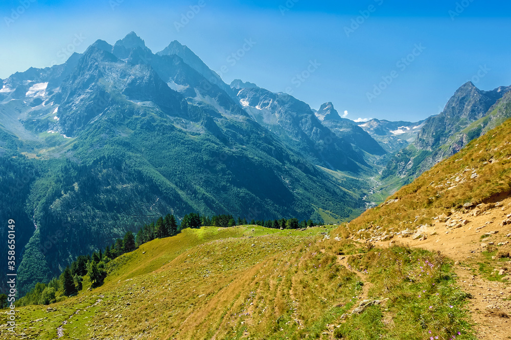 Hilly mountains against a cloudless blue sky. Snowy peaks. Coniferous forest in the foreground and the river in the distance. Tourism, travel, climbing, mountaineering. hike
