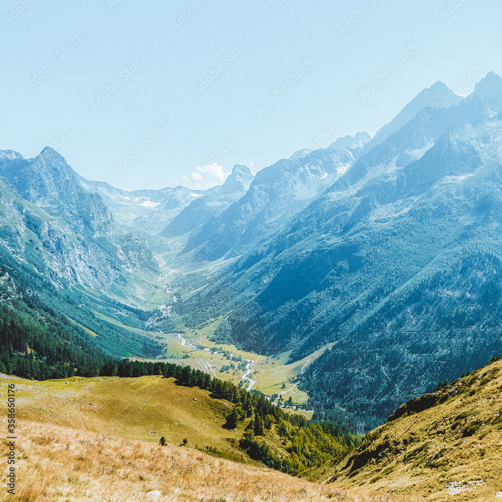 Hilly mountains against a cloudless blue sky. Snowy peaks. Coniferous forest in the foreground and the river in the distance. Tourism, travel, climbing, mountaineering. trekking
