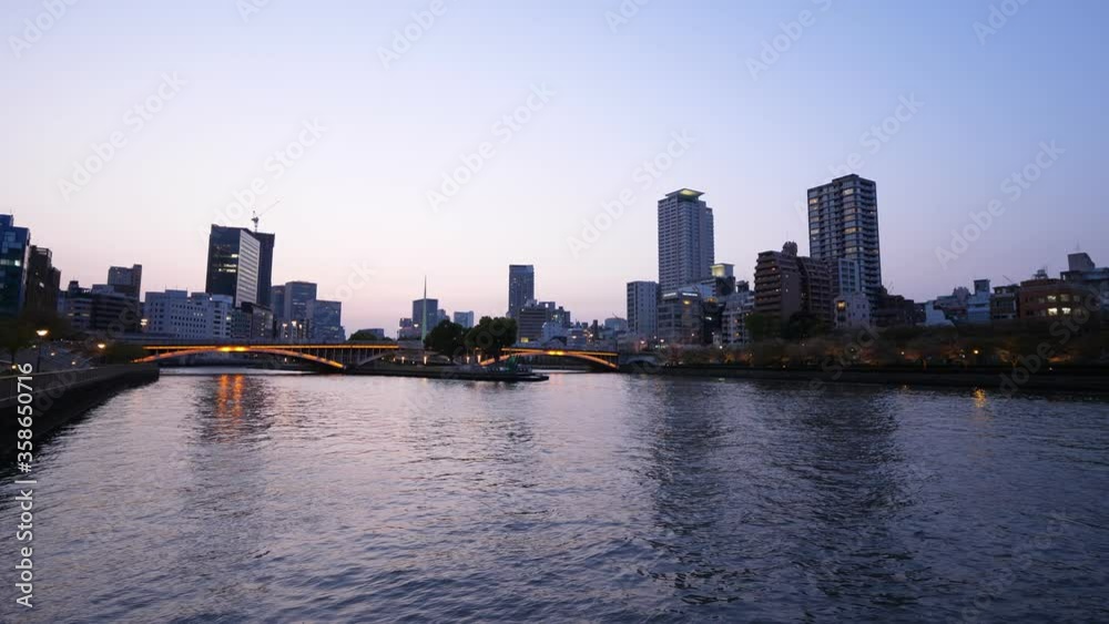 Okawa river panorama and illuminated Tenjin Bridge at blue hour, scenic views of Osaka city. Camera slowly turn right. Office and residential buildings seen around Okawa river panorama and illuminated Tenjin Bridge at blue hour, scenic views of Osaka city. Camera slowly turn right. Office and residential buildings seen around