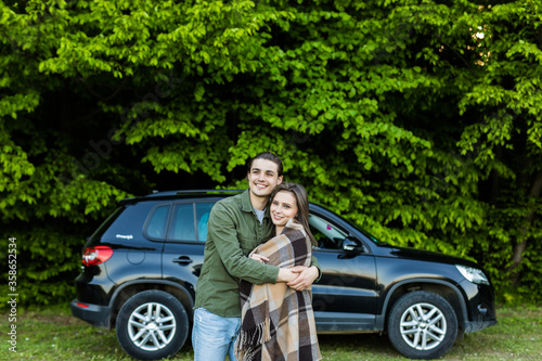 Beautiful young couple near car have a good time in the forest at daytime. Girl coveres by plaid. © F8  \ Suport Ukraine