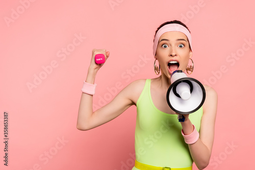 emotional sportswoman holding loudspeaker and dumbbell while screaming on pink © LIGHTFIELD STUDIOS