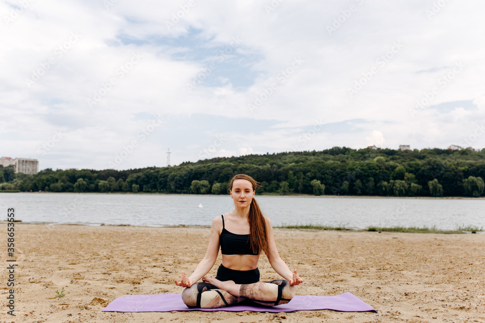 Young woman sitting on the beach in yoga pose
