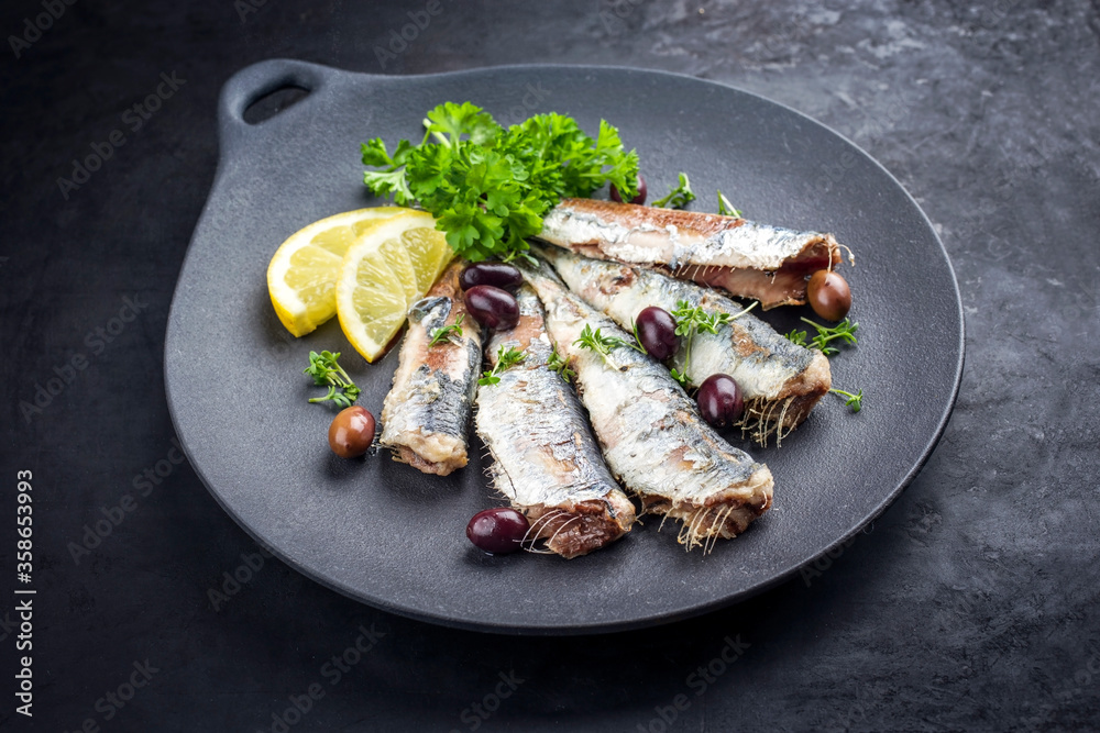 Fried sardines with lettuce and kalamata olives offered as closeup on a modern design plate with copy space Fried sardines with lettuce and kalamata olives offered as closeup on a modern design plate with copy space