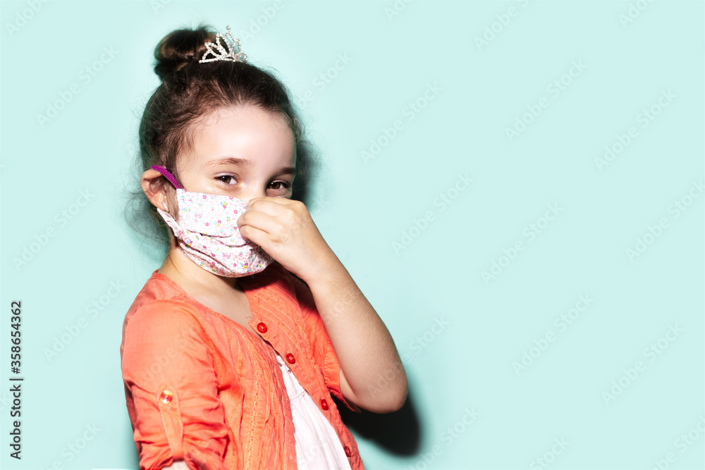 Studio portrait of child girl wearing medical flu mask on face against coronavirus on background of aqua menthe color with copy space.
