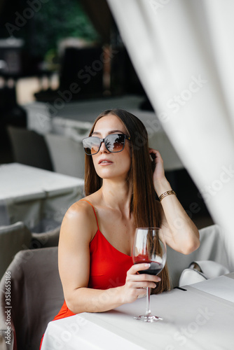 Beautiful young girl sits and drinks wine on the veranda of a beautiful house. Holiday.