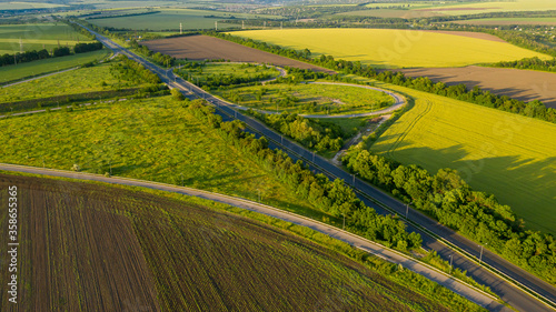 Flight over highway amid meadow on summer sunny day. Beautiful countryside landscape scenery from drone view. Aerial view photo of the road amid field.