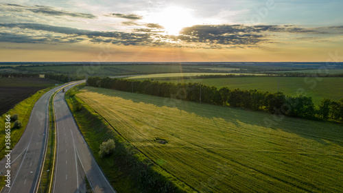 Aerial view photo of the road amid field. Flight over highway amid meadow on summer sunny day. Beautiful countryside landscape scenery from drone view.