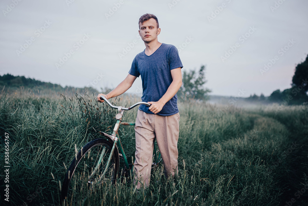 man walks with a green retro bicycle on a field road and grass in summer. man walks with a green retro bicycle on a field road and grass in summer.