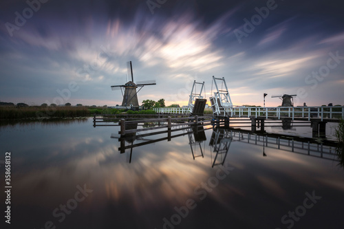 Holland, Kinderdijk - open-air museum of windmills standing on the banks of canals. A lifting, white, wooden bridge leads from the windmill across the canal. Evening romance. © Jana Krizova