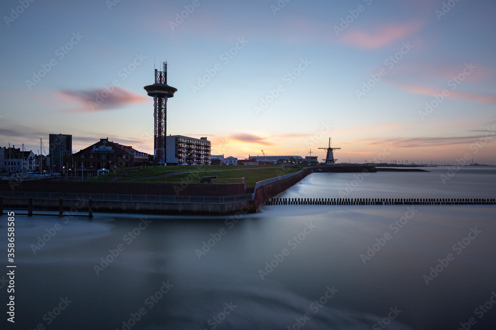 Vlissingen - morning view of the harbor. To the left is a tall observation tower, in the background a windmill and a harbor. It calmed the sea level for a long time.