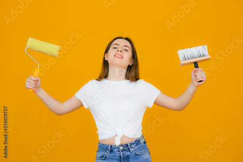 beautiful young satisfied woman with roller and brush on yellow background. Painter women at work, with roller painting wall, painter house concept