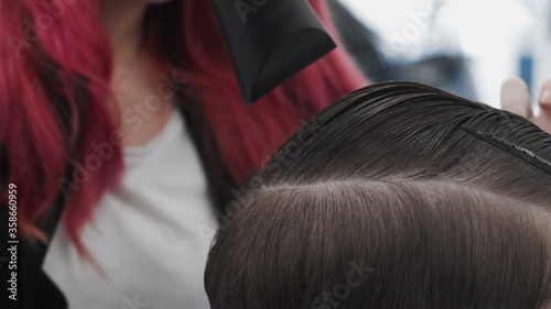 Professional female hairstylist dries male hair in hair salon