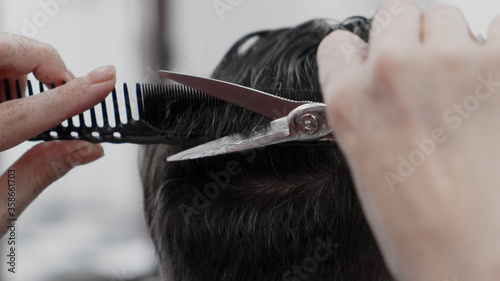 Professional female hairstylist combing and cutting man hair