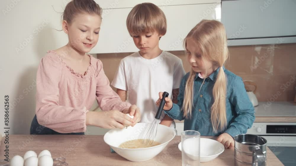 Beautiful blond children make dough together. Beat the eggs in a white plate Beautiful blond children make dough together. Beat the eggs in a white plate