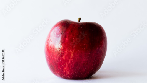 Plano frontal de una rojiza y fresca manzana completamente aislado sobre un fondo totalmente blanco con luz natural sobre ella