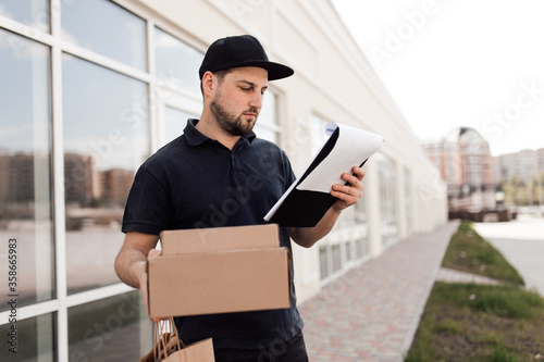 Portrait of courier with order papers and packages with food near door © Olena