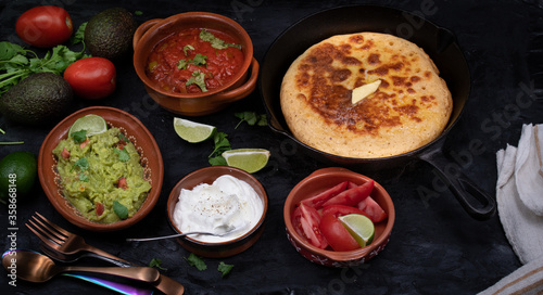 Mexican skillet cornbread served with tomato salsa and guacamole, sour cream on dark table