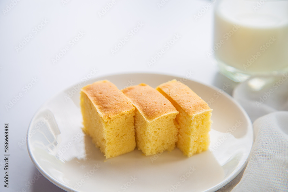 Close up a sliced butter cake in a white plate non a white table with a cup of milk blurred background.