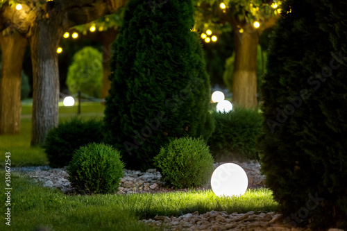 Foto backyard light garden with lantern electric lamp with a round diffuser in the green grass with thuja bushes in a park with landscaping, closeup night scene nobody