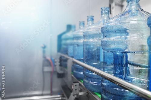 Water bottling conveyor line with plastic bottles or gallons on water factory production, selective focus for copy space.