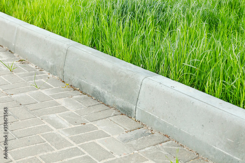 A curbstone separates the pedestrian zone from the green tall grass of the lawn. City improvement photo