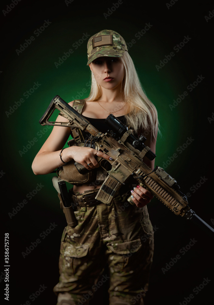 a sexy girl in military airsoft overalls poses with a gun in her hands on a dark background