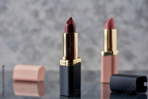Lápiz labial Rojo con negro y rosa sobre una superficie de mármol con las tapas tiradas al costado  y una composición elegante y espacio para texto