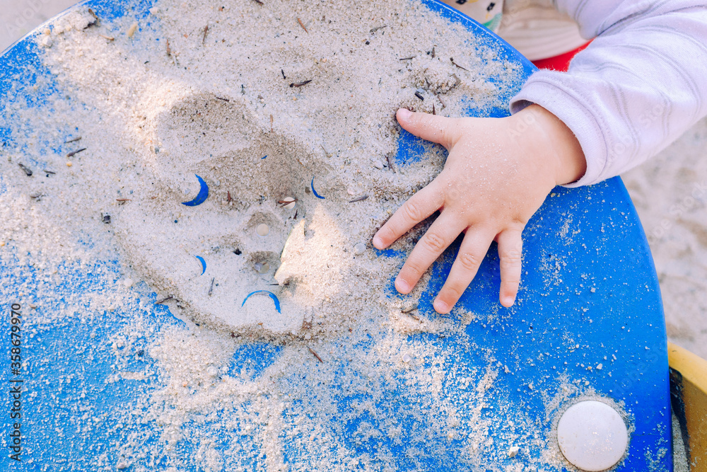 A baby's hand checking the texture of the sand in a playground.