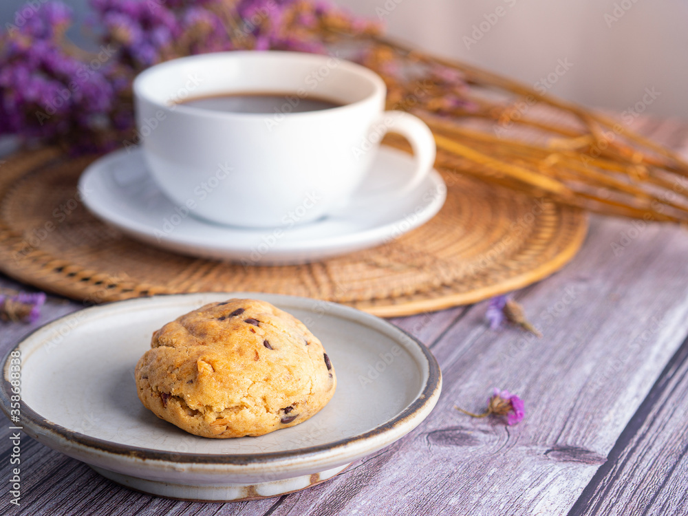 Close-up of a cookie on a plate with a white coffee cup and flower blurred background. Space for text. Close-up of a cookie on a plate with a white coffee cup and flower blurred background. Space for text.