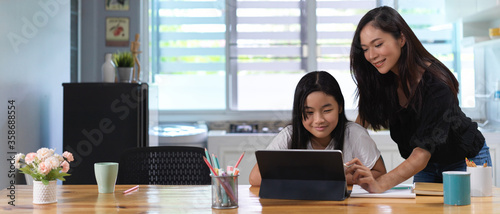Принти на полотні Mother helping her daughter do homework with digital tablet on wooden worktable