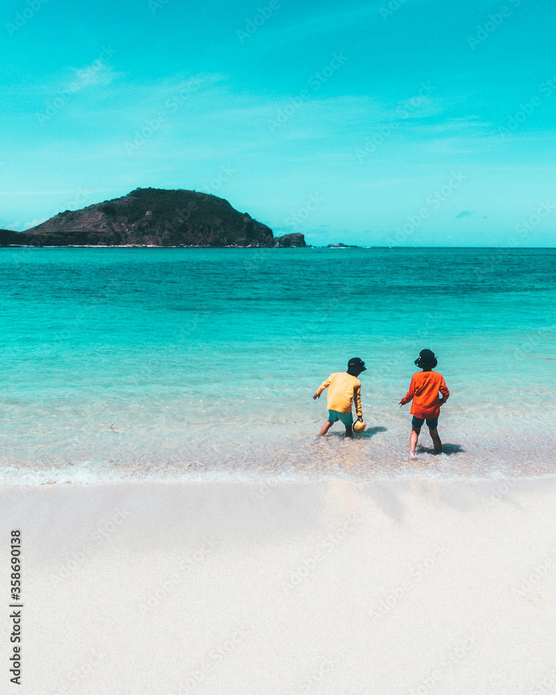 Two kids playing on the beach on summer holidays. Children in nature with beautiful sea, sand and blue sky. Happy kids on vacation playing on the water in Lombok Island, Indonesia