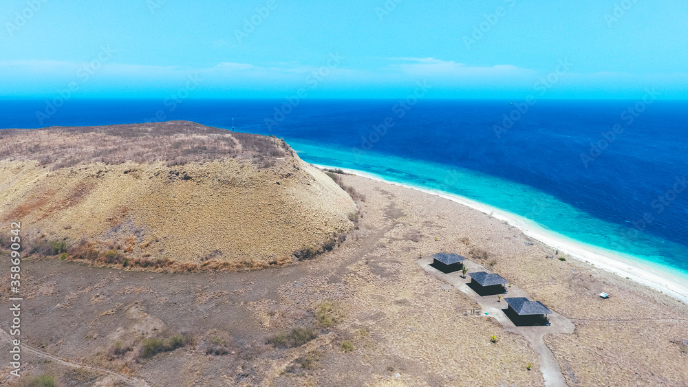 Beautiful summer island with dry grass. Paserang Island in West Sumbawa, Indonesia. The yellow land with small hill and blue sky. Aerial image captured by drone.