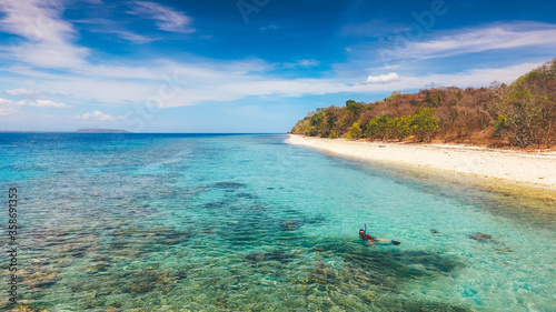 Aerial drone view of an empty white sandy beach with a man snorkeling in tropical Moyo Island  Sumbawa  Indonesia