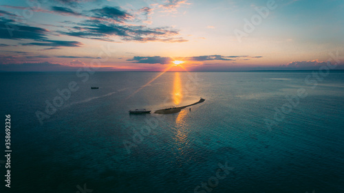 Beautiful sunset at the sea in Takat Sagele, Moyo Island, Sumbawa, Indonesia. Silhouette of a small island on a background of horizon separated orange and turquoise sky from the blue surface of water photo