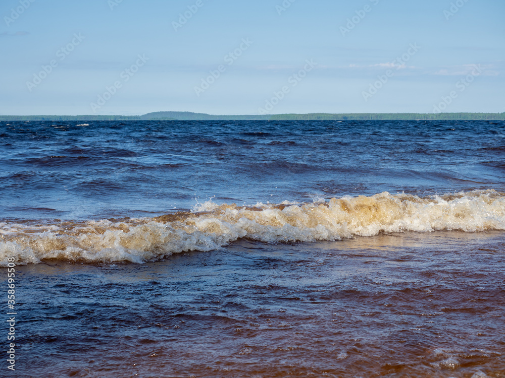 Waves with white foam on a lake with shallow depth in a sunny, windy day in Karelia, northwest of Russia