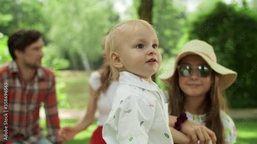 Sister and toddler looking at camera outdoors. Family relaxing together in park Sister and toddler looking at camera outdoors. Family relaxing together in park