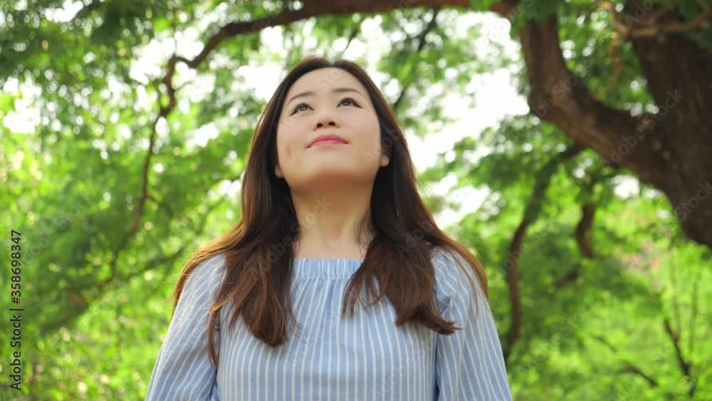 Asian woman takes off mask and exhaling fresh air. End of during Coronavirus COVID-19 Epidemic, The coronavirus pandemic is over, Mask on off outside in green park. Asian woman takes off mask and exhaling fresh air. End of during Coronavirus COVID-19 Epidemic, The coronavirus pandemic is over, Mask on off outside in green park.