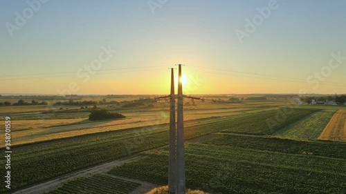 Drone fly close to transmission electricity concrete pylon tower during sunset over an agricultural field in the farm on countryside photo