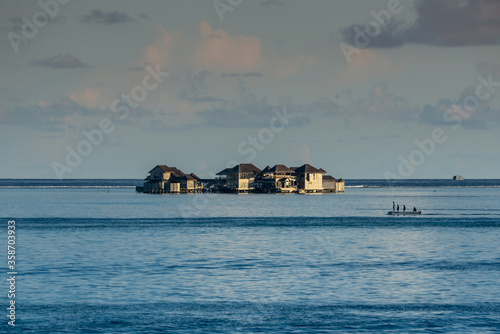 Wooden houses in middle of water, small boat with people in the ocean at early evening sunset time in tropical islands in Indian Ocean in Maldives