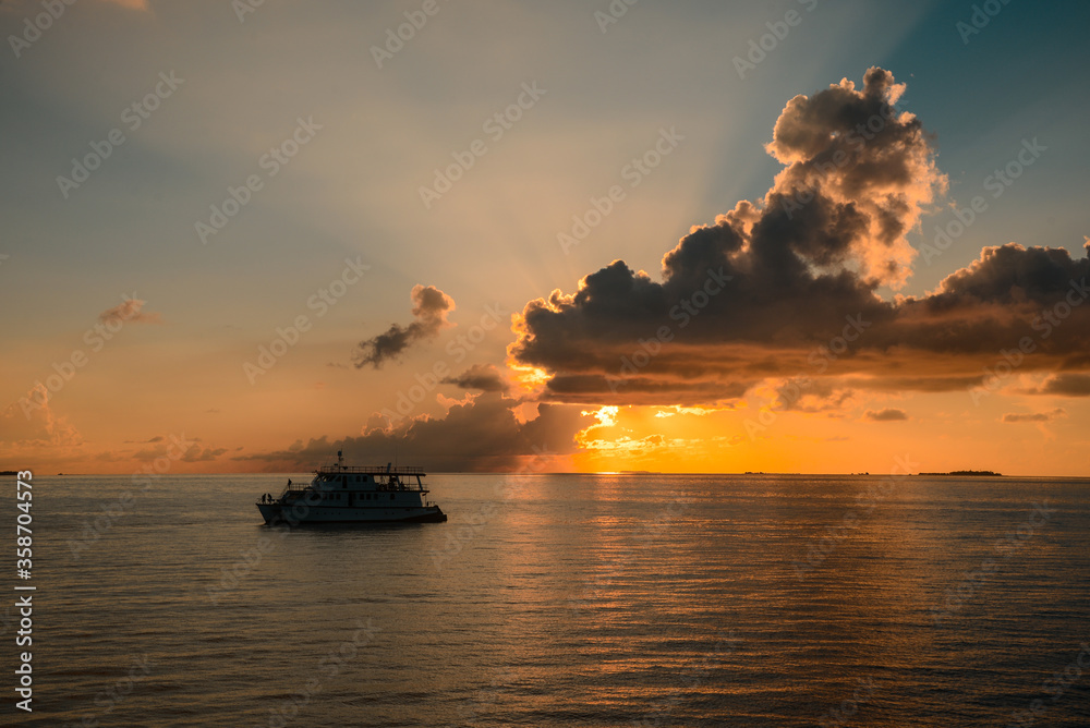 Colourful sunset in tropical islands with yacht, yellow clouds and sun rays