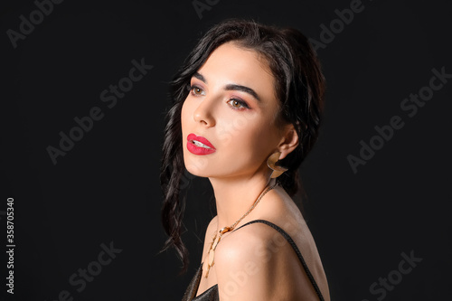 Beautiful young woman wearing stylish jewelry on dark background