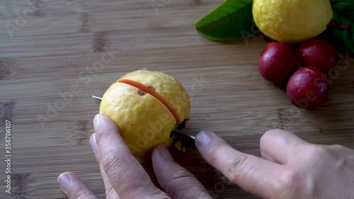 Hands slice ripe yellow apple guava fruit with knife revealing pink inside photo