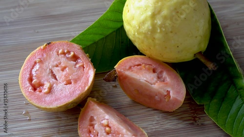 Whole and halved yellow guava with pink inside cut into slices on wood background photo