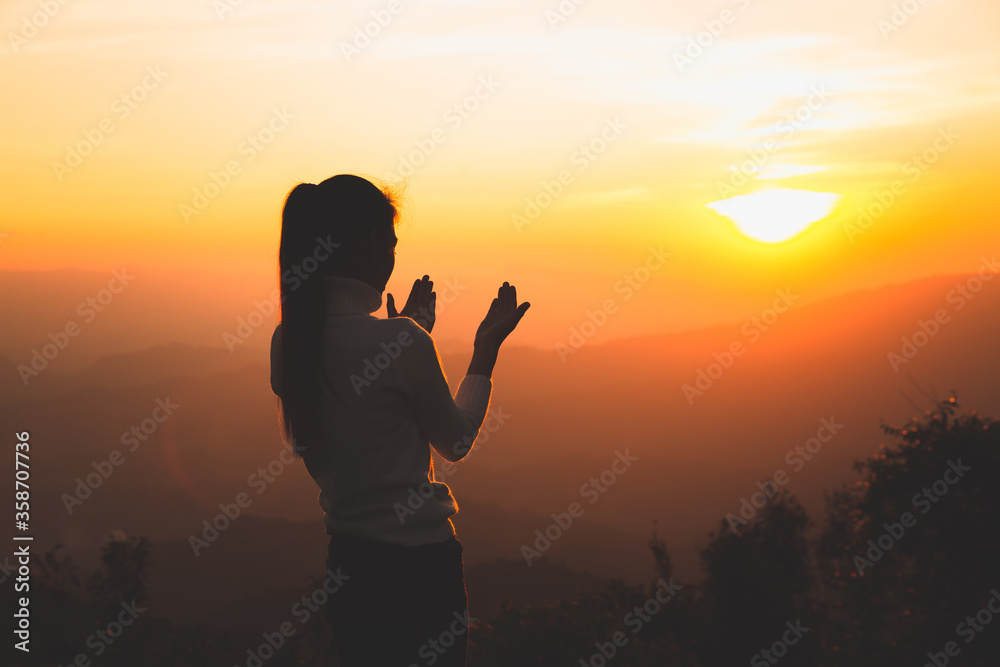 A women is praying to God on the mountain. Praying hands with faith in religion and belief in God on blessing background. Power of hope or love and devotion.